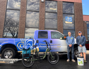 Two white men standing in front of Annapolis Compost bike and Oyster Recovery Partnership truck and office. Bucket of oyster shells on ground with ORP and Annapolis Compost logo.