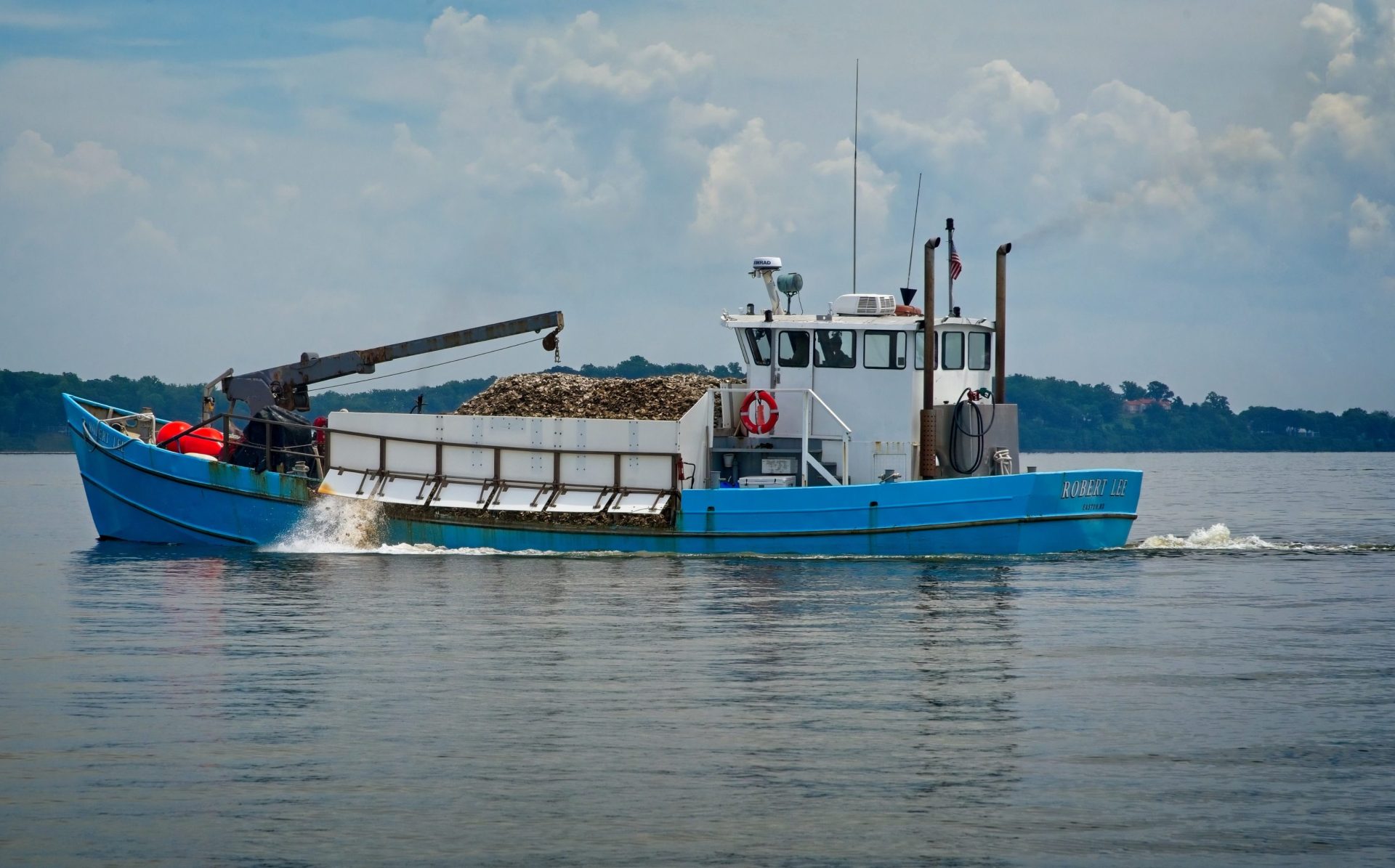 Blue boat spraying oysters over the side.